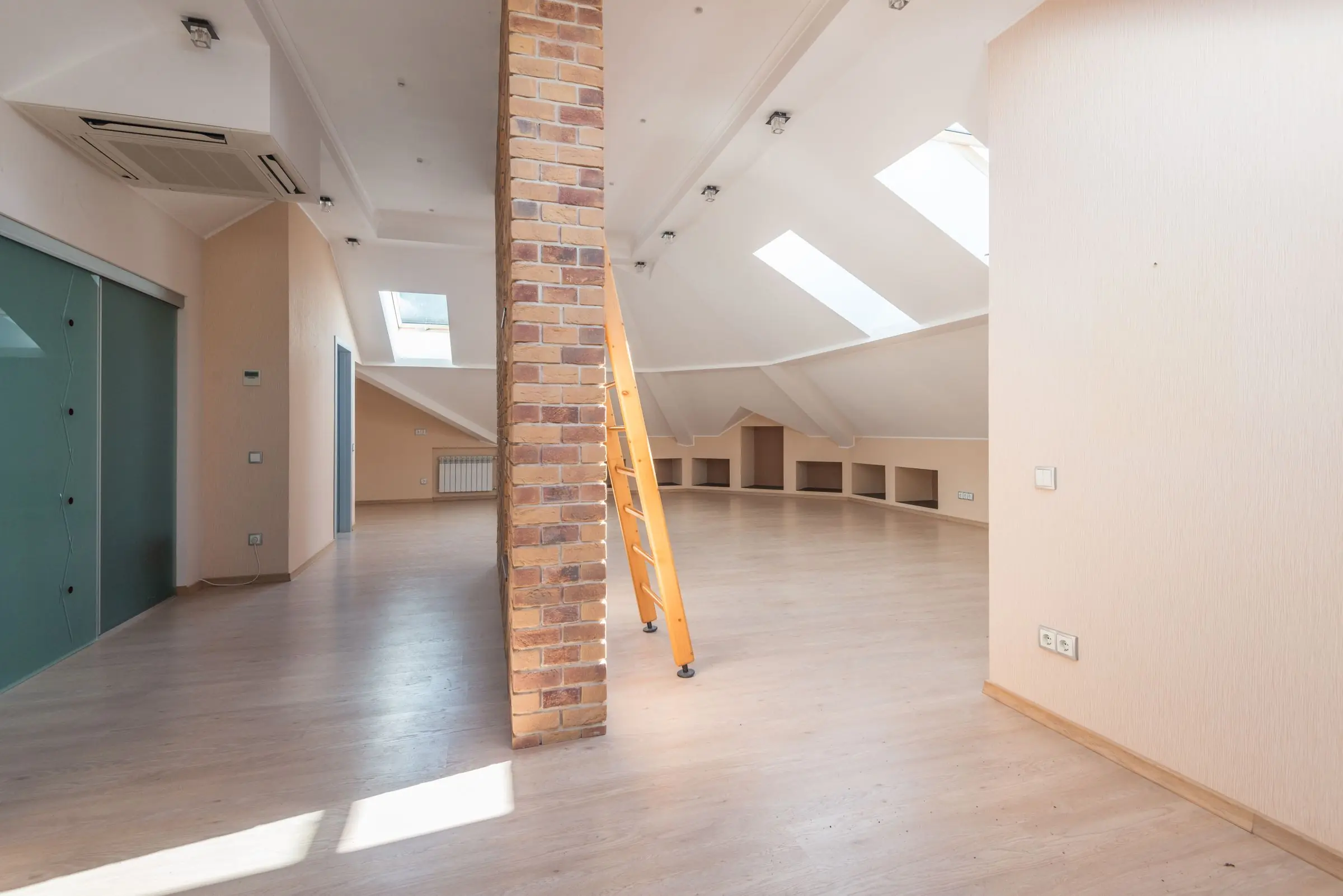 Des combles aménagés et lumineux, avec des fenêtres de toit, un pilier de briques et un parquet clair